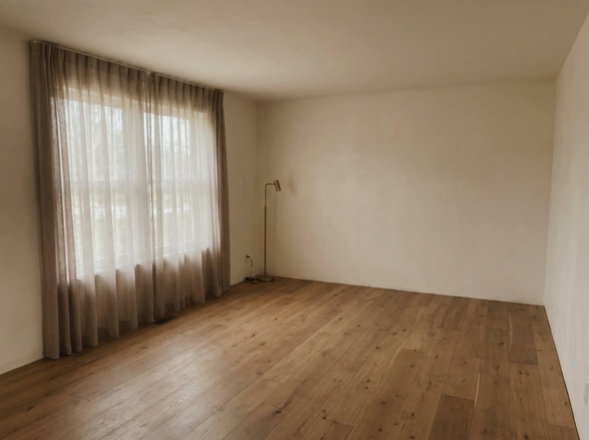 Empty room with sheer curtains and a bare timber floor, then the same room holding a curved cream sofa and a round table, vacant