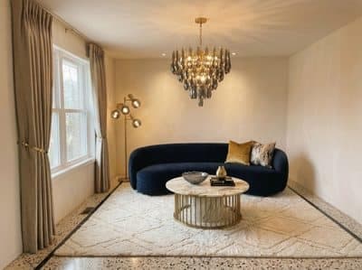 The same living room with a navy velvet sofa, marble and brass coffee table and a crystal chandelier