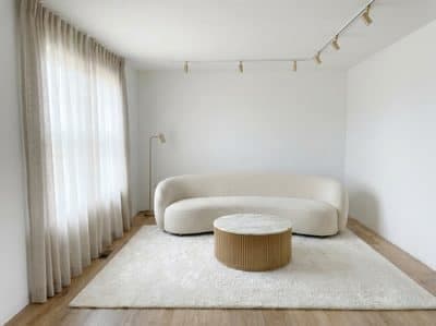Living room with a curved cream boucle sofa, round oak coffee table and pale rug beside a linen-curtained window